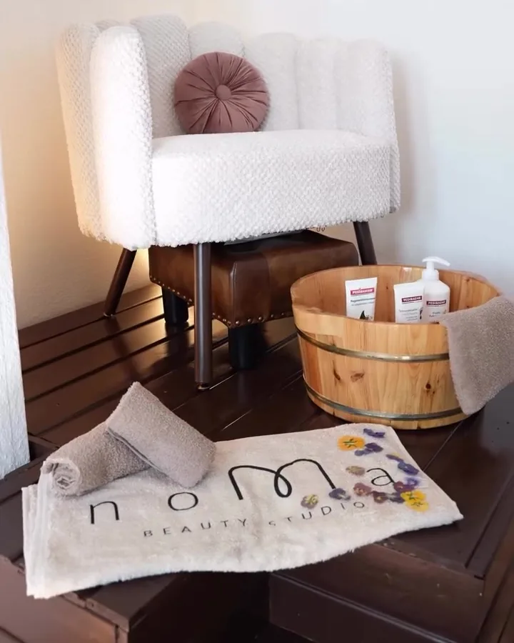 Bouclé-Sessel mit altrosa Kissen, daneben ein Holzzuber für das Foot Spa und ein Handtuch mit dem gestickten noMa-Logo
